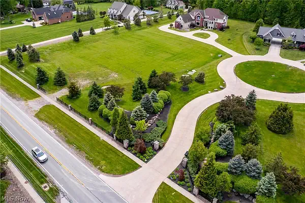 An aerial view of a large, manicured residential lot featuring a winding concrete driveway that leads from a main road into an upscale suburban neighborhood.