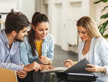 A young couple sitting together and reviewing documents in a folder with a female professional in a bright office setting.